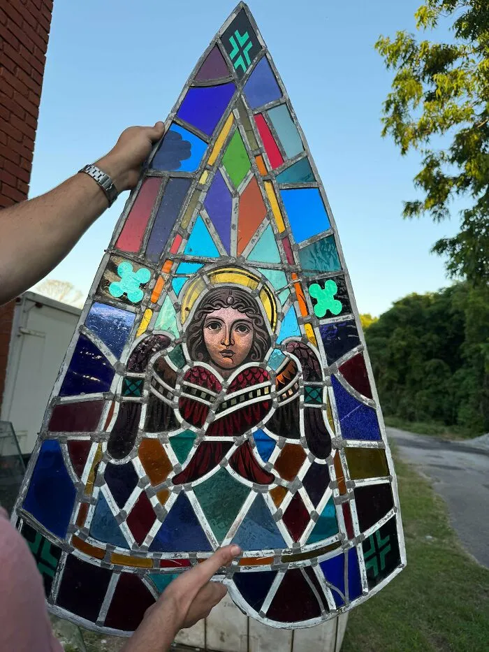 A person holding a large triangular antique stained glass window panel depicting an angel