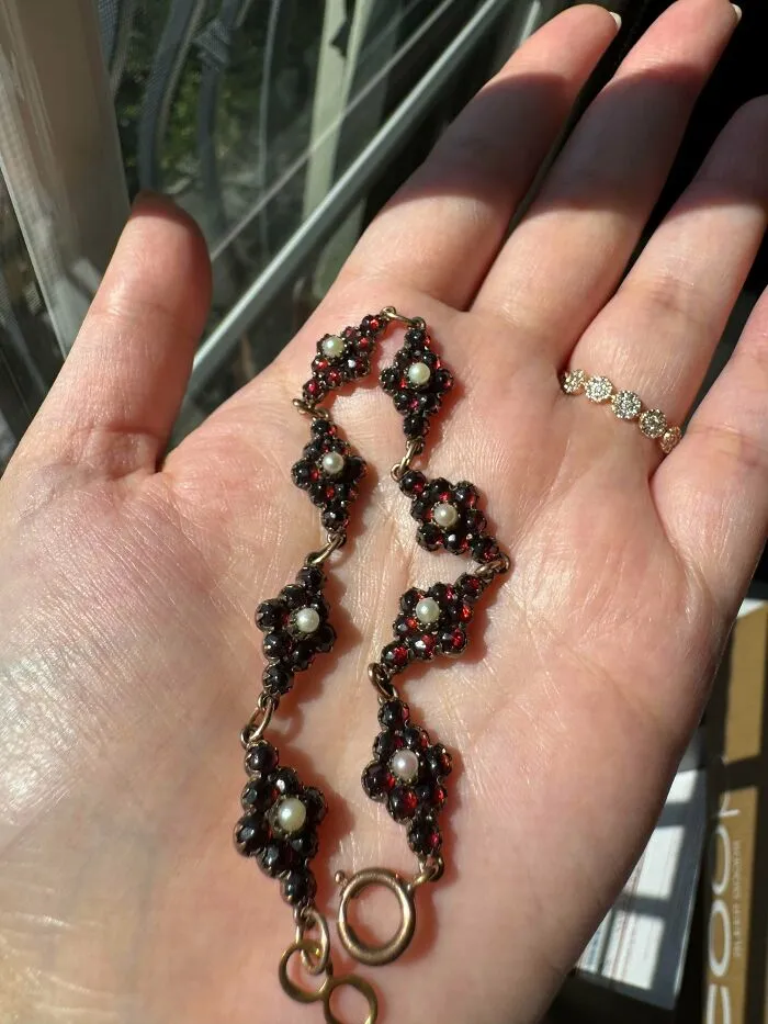 An ornate vintage bracelet with red gemstones and pearls held in an open hand, a find for antique lovers.
