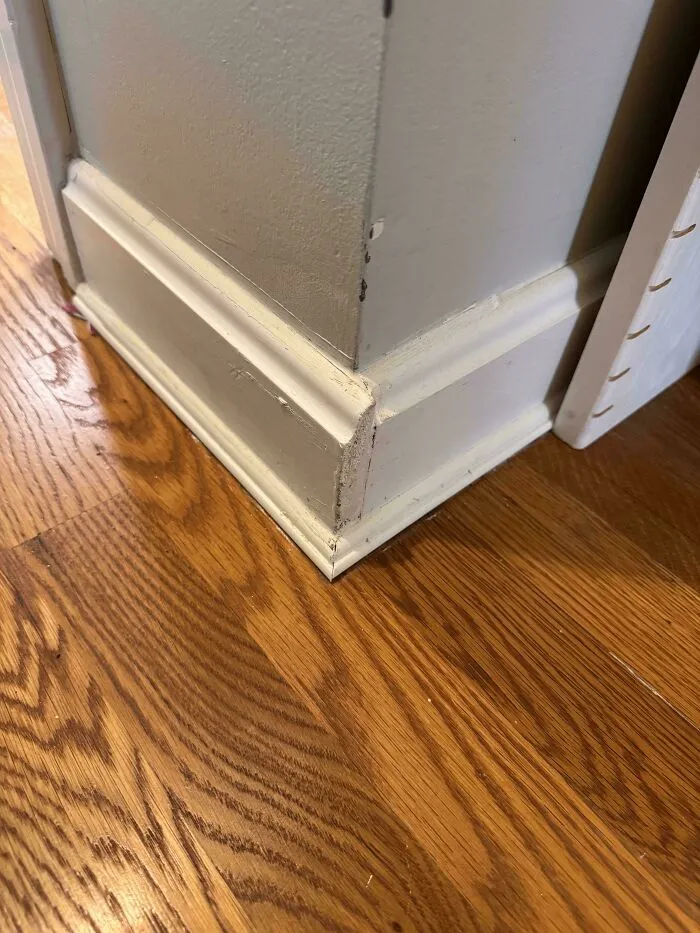 A questionable DIY project showcasing poorly aligned baseboard molding on a home wall corner.