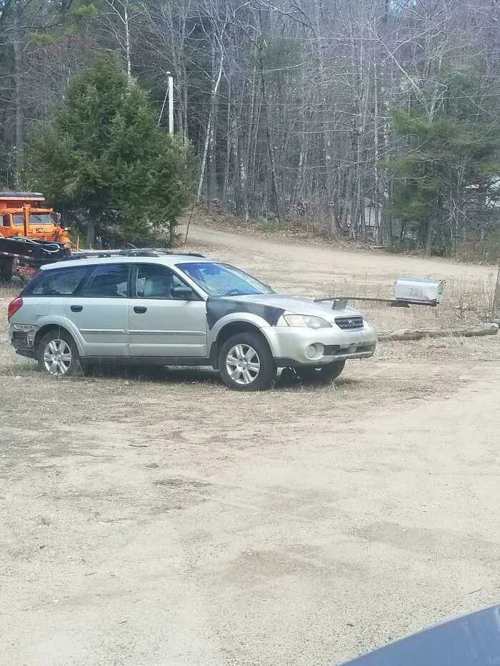 A questionable DIY project showing a silver station wagon car parked near a woodland road with a front hood mod.