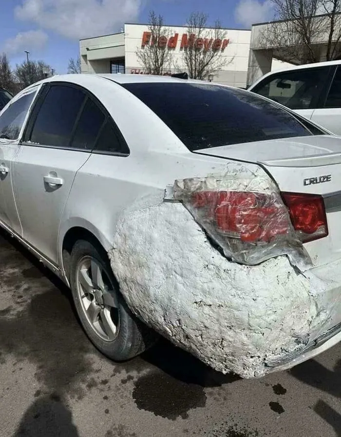 A questionable DIY project featuring a car with its rear bumper poorly repaired with spray foam and tape.