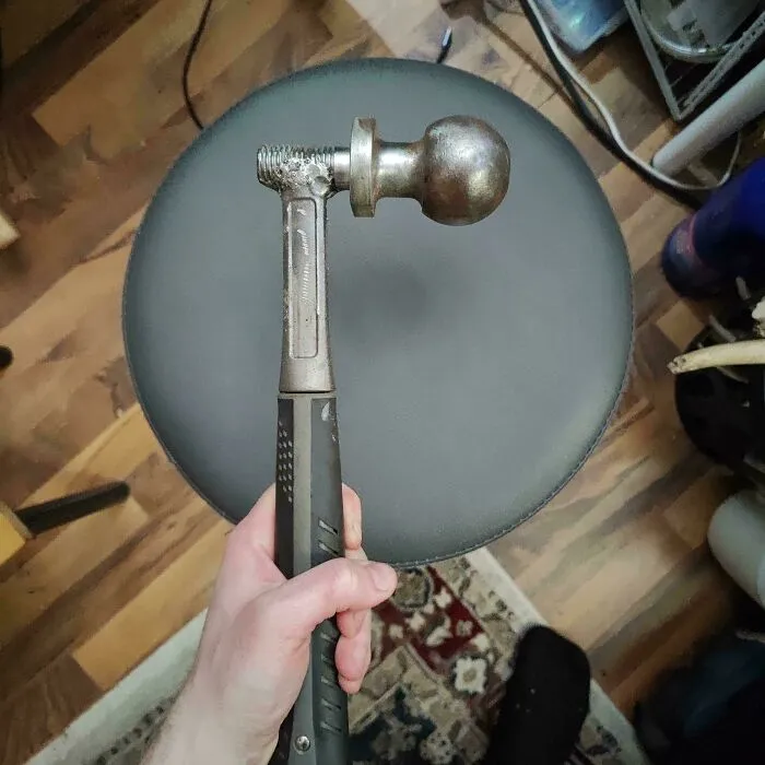 A hand holding a hammer modified with a trailer hitch ball as a questionable DIY project