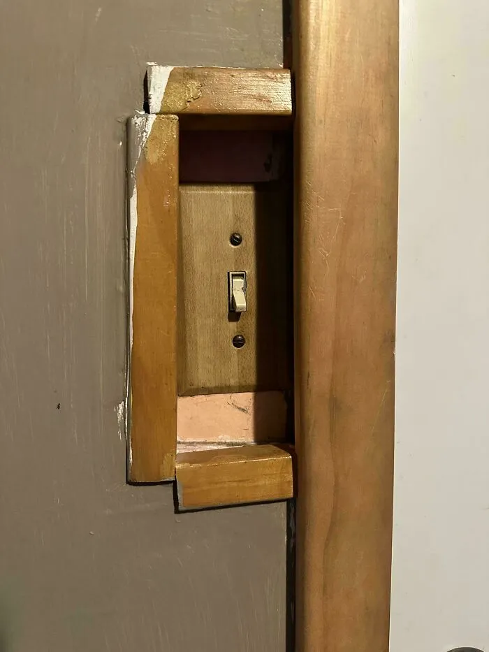 A poorly fitted wooden frame around a wall light switch, highlighting questionable DIY projects.