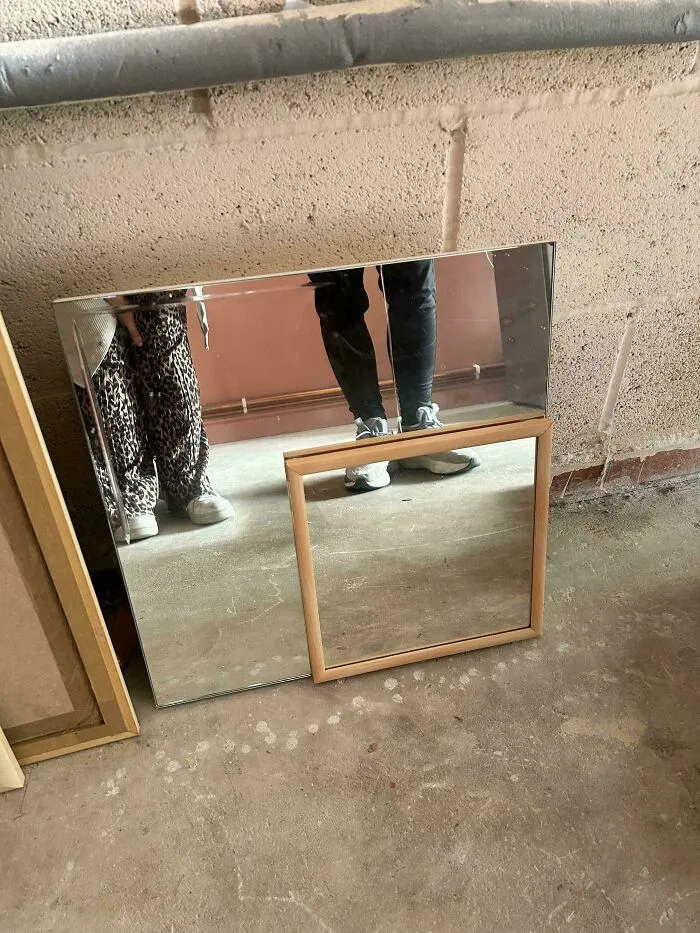 A questionable DIY mirror project with a smaller framed mirror attached to a larger one on a concrete floor.