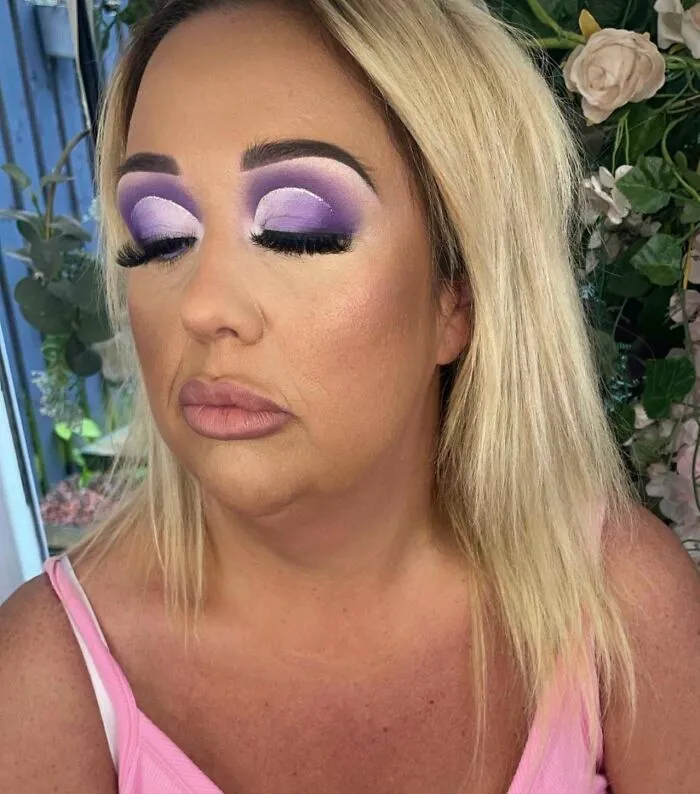 A woman with excessively dramatic purple eyeshadow and poorly sculpted eyebrows after a beauty salon visit.