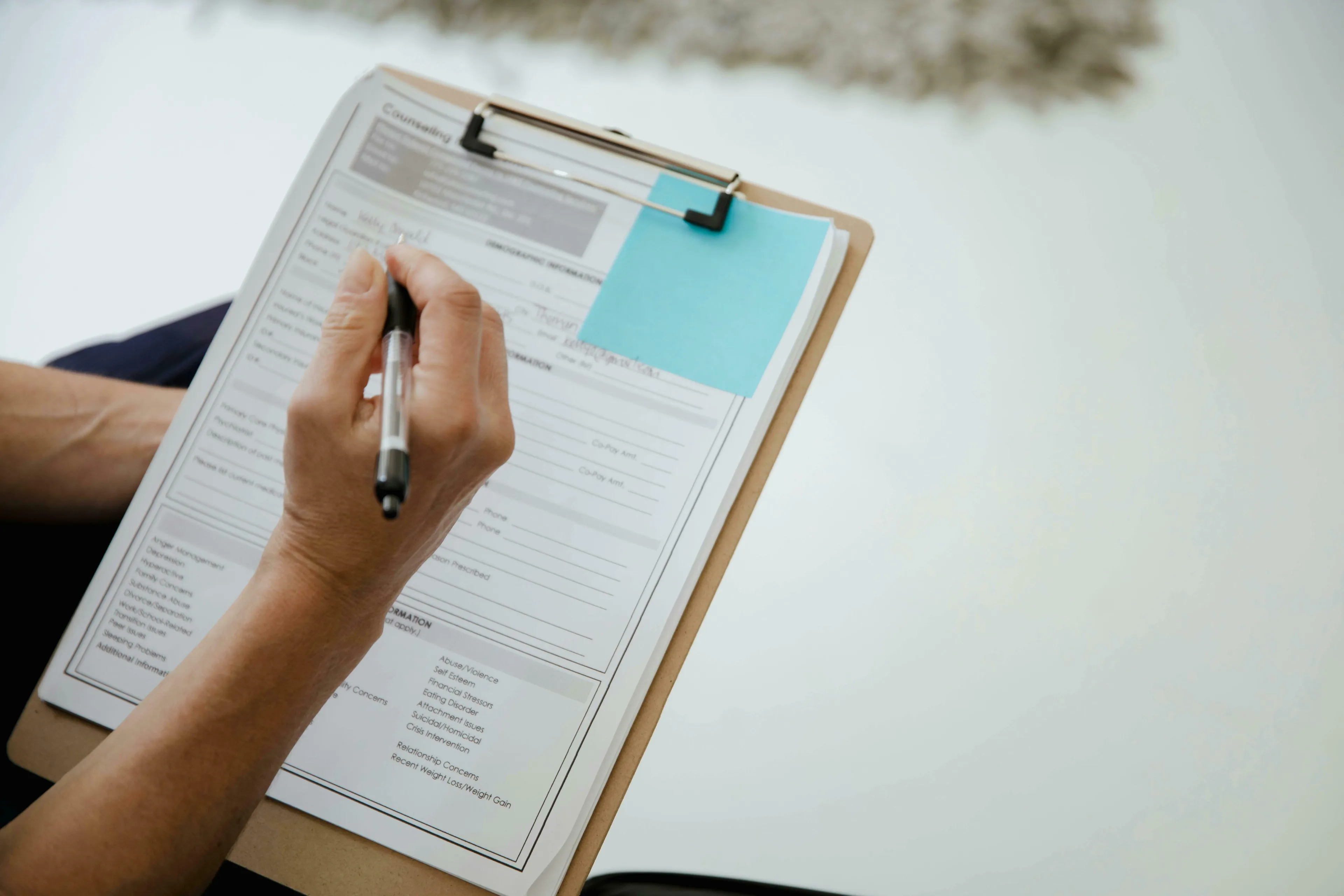 A person's hand writing with a pen on a clipboard, practicing correct spelling of English words.