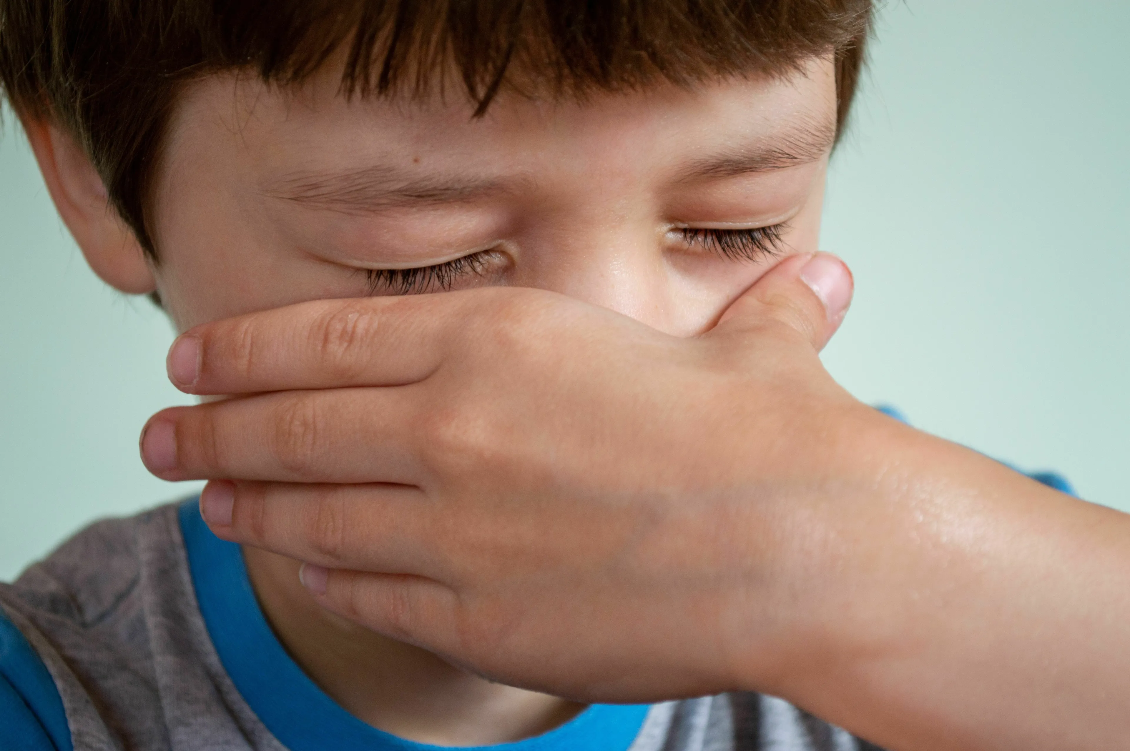 A young boy covers his mouth and closes his eyes, possibly feeling shy or embarrassed about English words spelling.