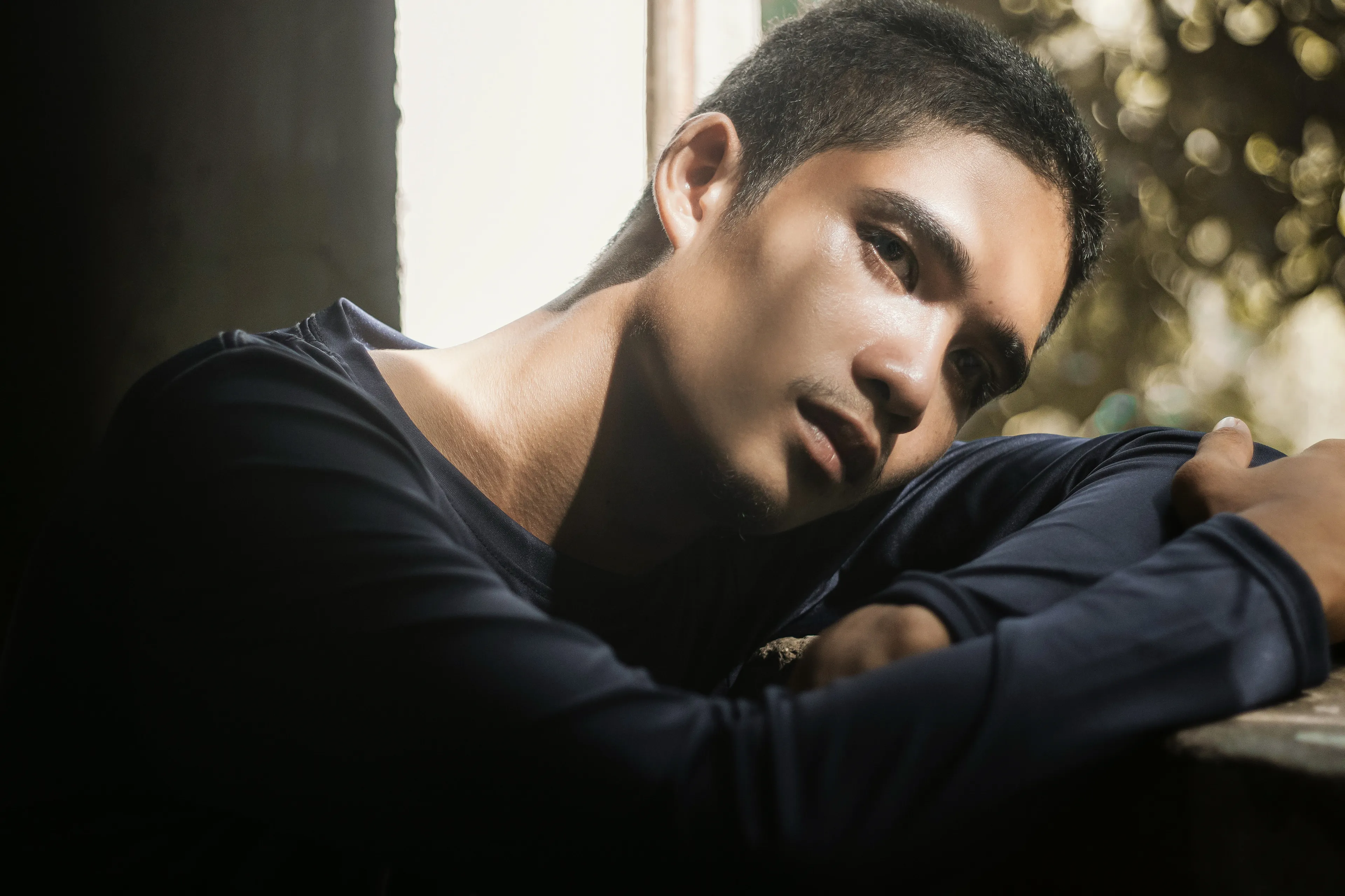 A pensive man, leaning, sunlight highlighting his face. He seeks to experience joy and come back to himself.