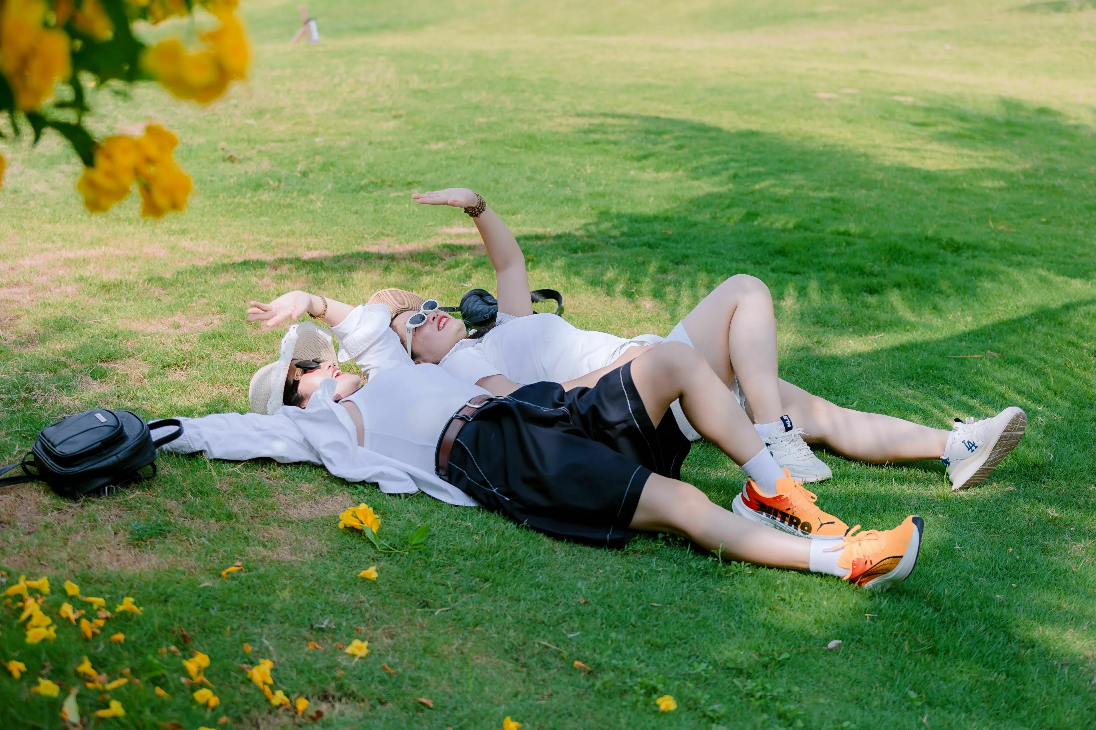 Two women lying on green grass under a tree, enjoying the sun. They experience joy in nature.