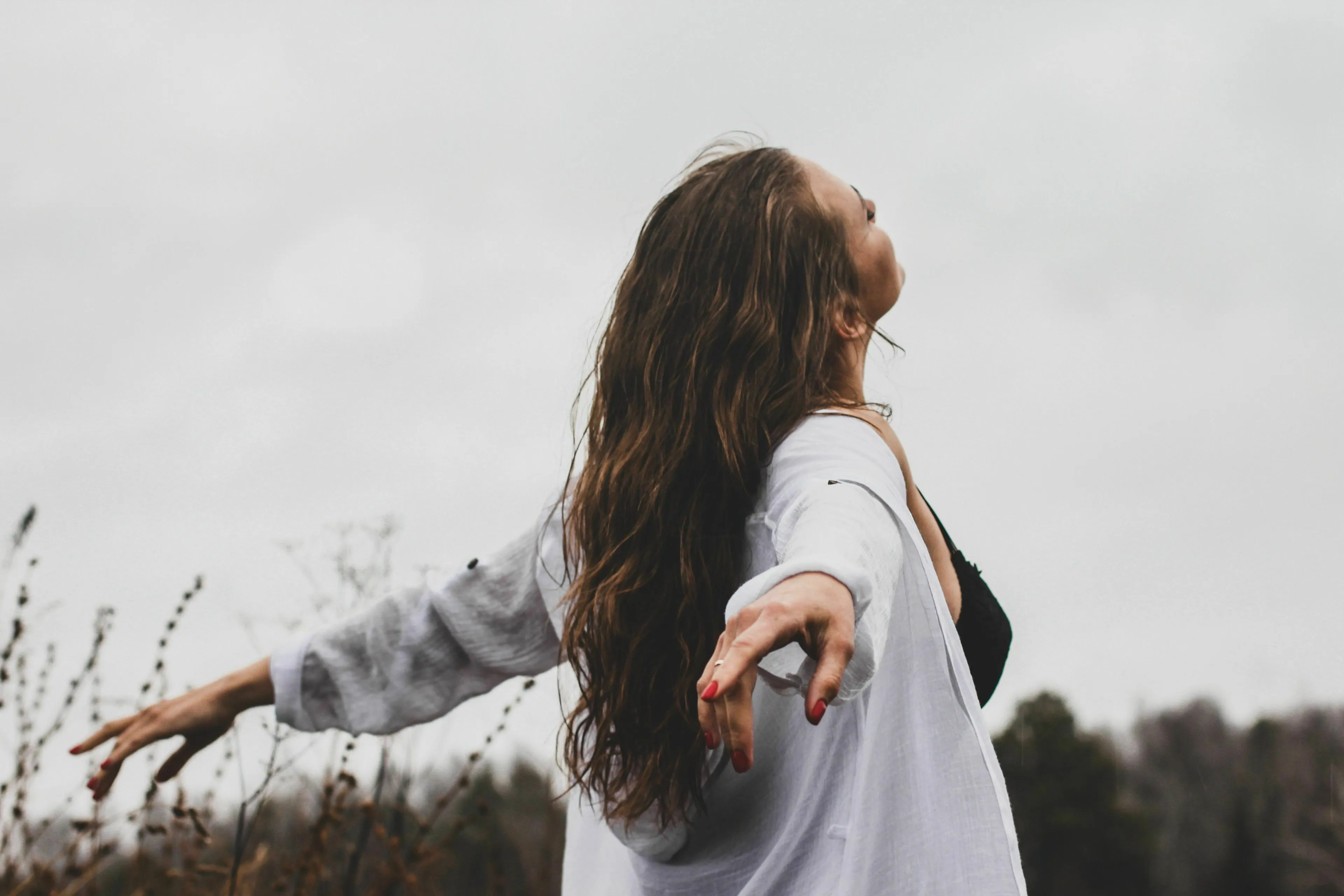 Woman with arms outstretched, looking skyward, feeling alive and experiencing joy outdoors.