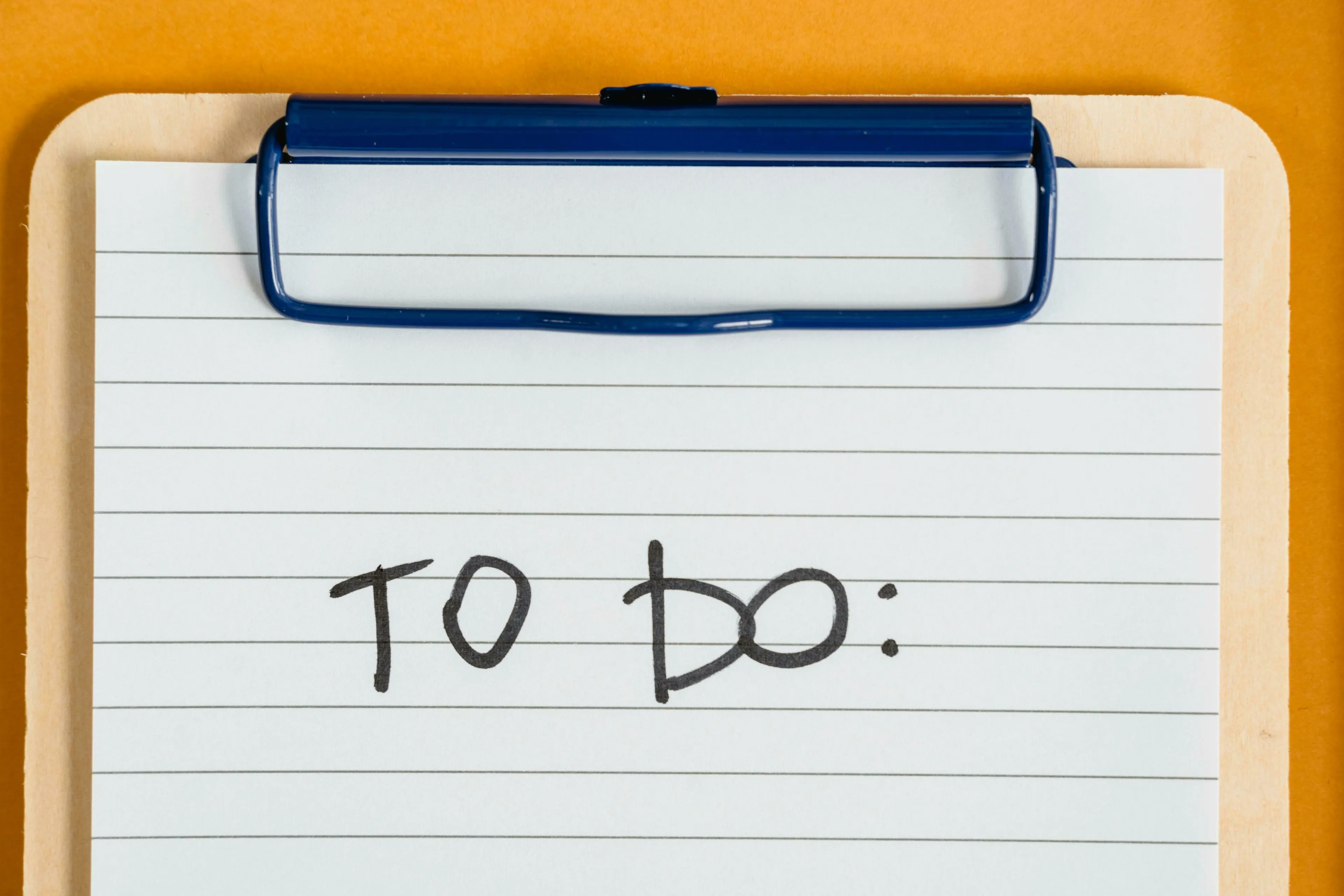 A lined piece of paper on a clipboard with 'TO DO:' written on it. Explore how to-do lists affect joy.