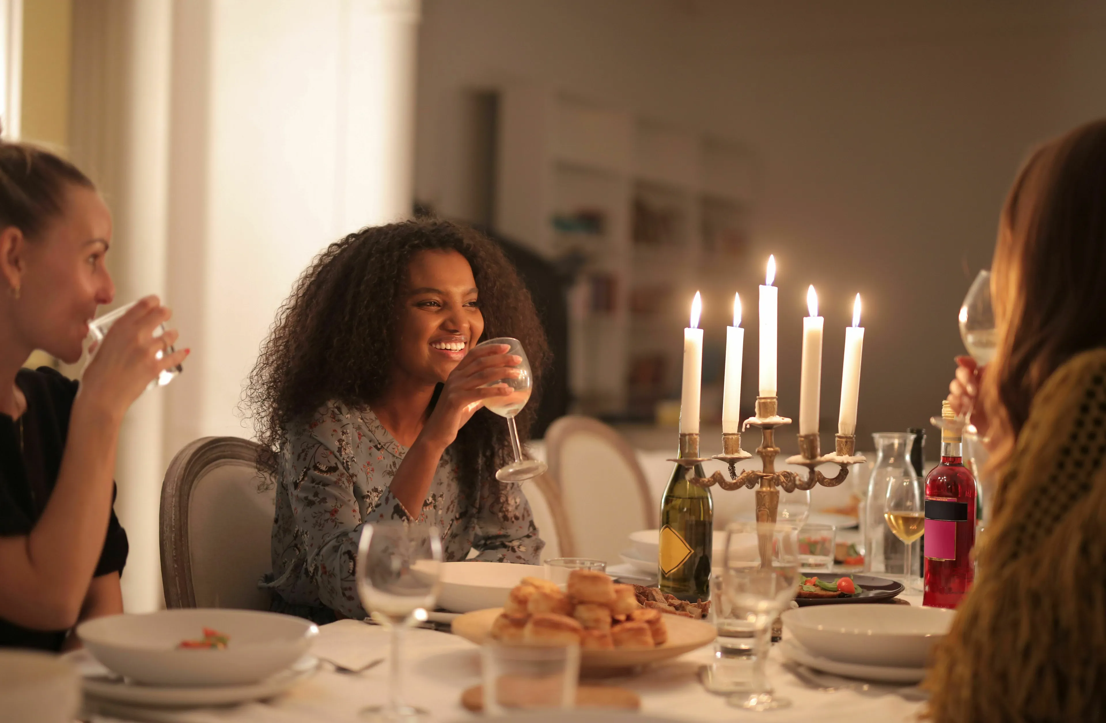 Smiling woman with curly hair enjoys an ideal dinner party, experiencing joy with friends by candlelight.