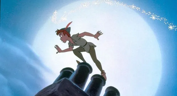 Peter Pan, an animated movie character, running across cannon tops with pixie dust trailing behind him against a bright blue sky.