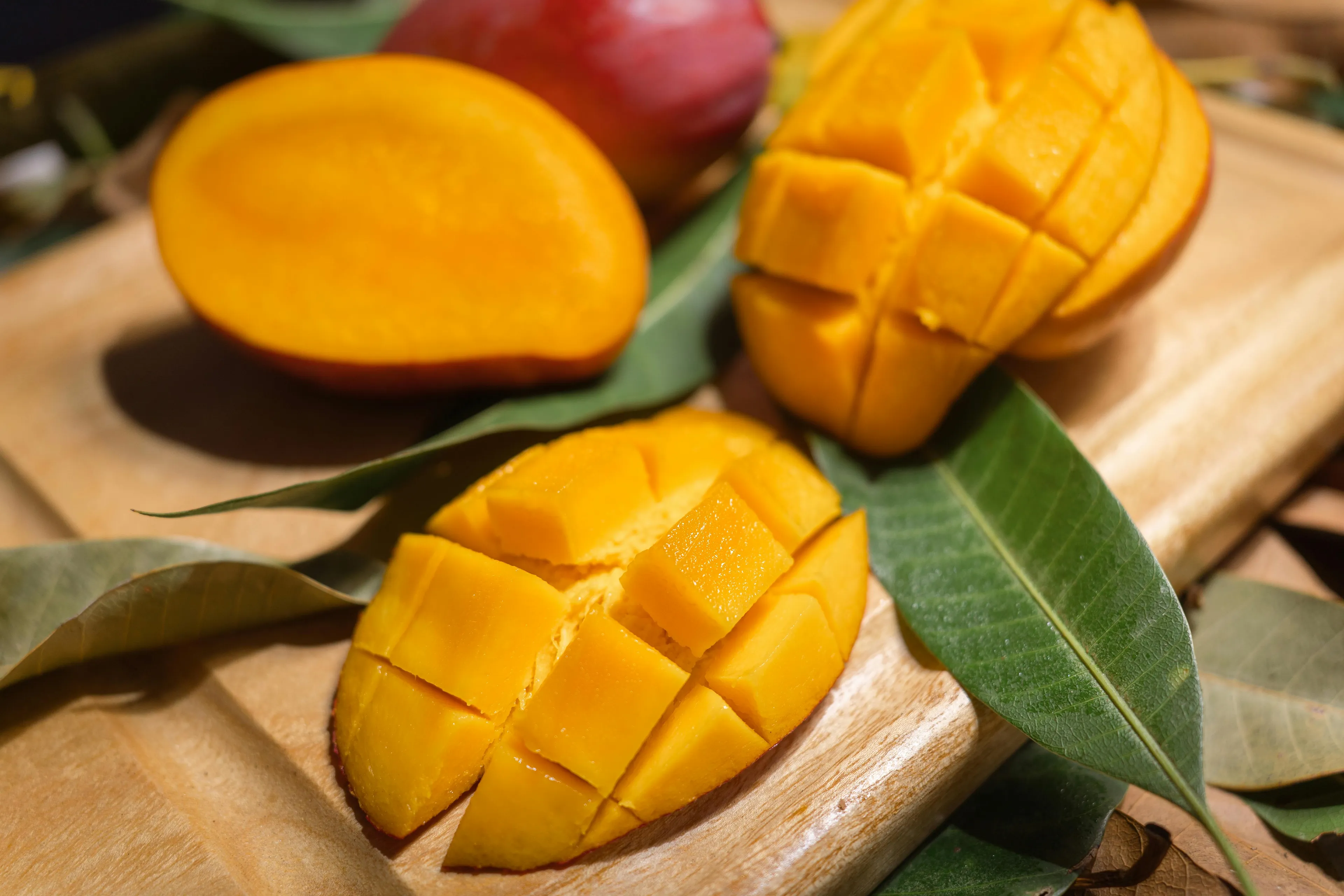 Bright yellow mango, sliced and cubed, with a whole red mango in the background. A delicious snack on a wooden board.