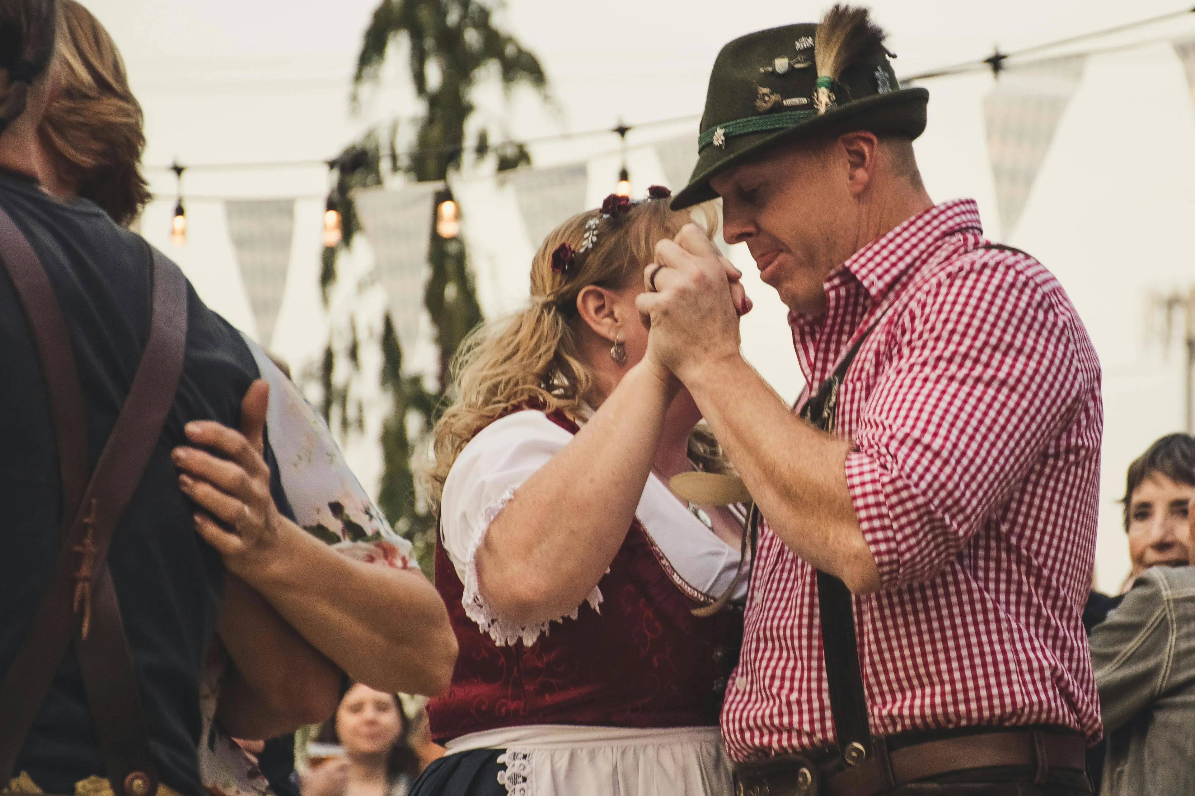 A couple in traditional Bavarian attire dancing closely, celebrating Oktoberfest. The man wears a trachtenhut and lederhosen.