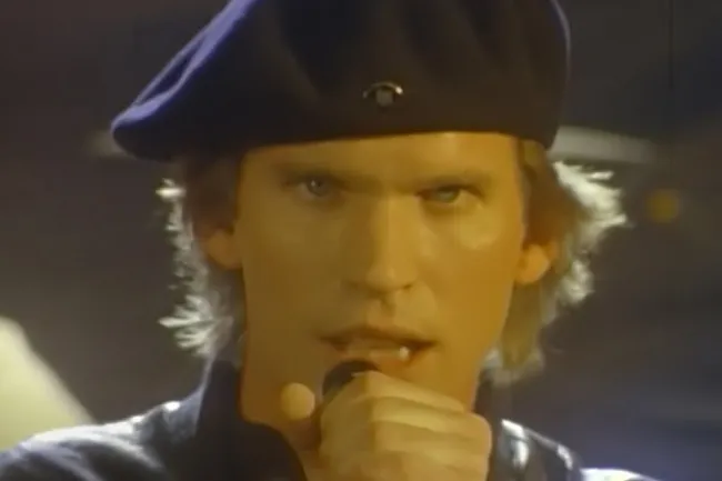 A man wearing a beret and singing into a microphone, embodying the joy of music, perhaps Eye of the Tiger.