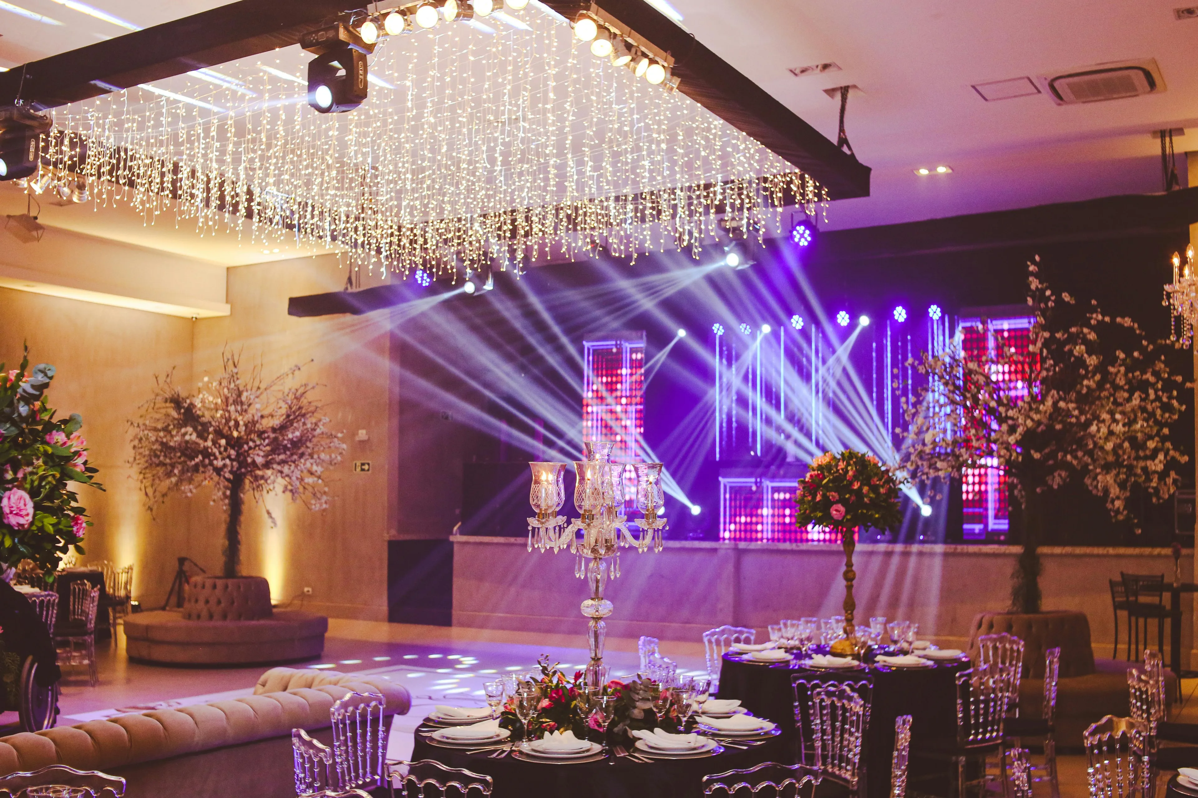 A glamorous event space with sparkling lights, elegant table settings, and a stage with purple spotlights. Ideal for event planning.
