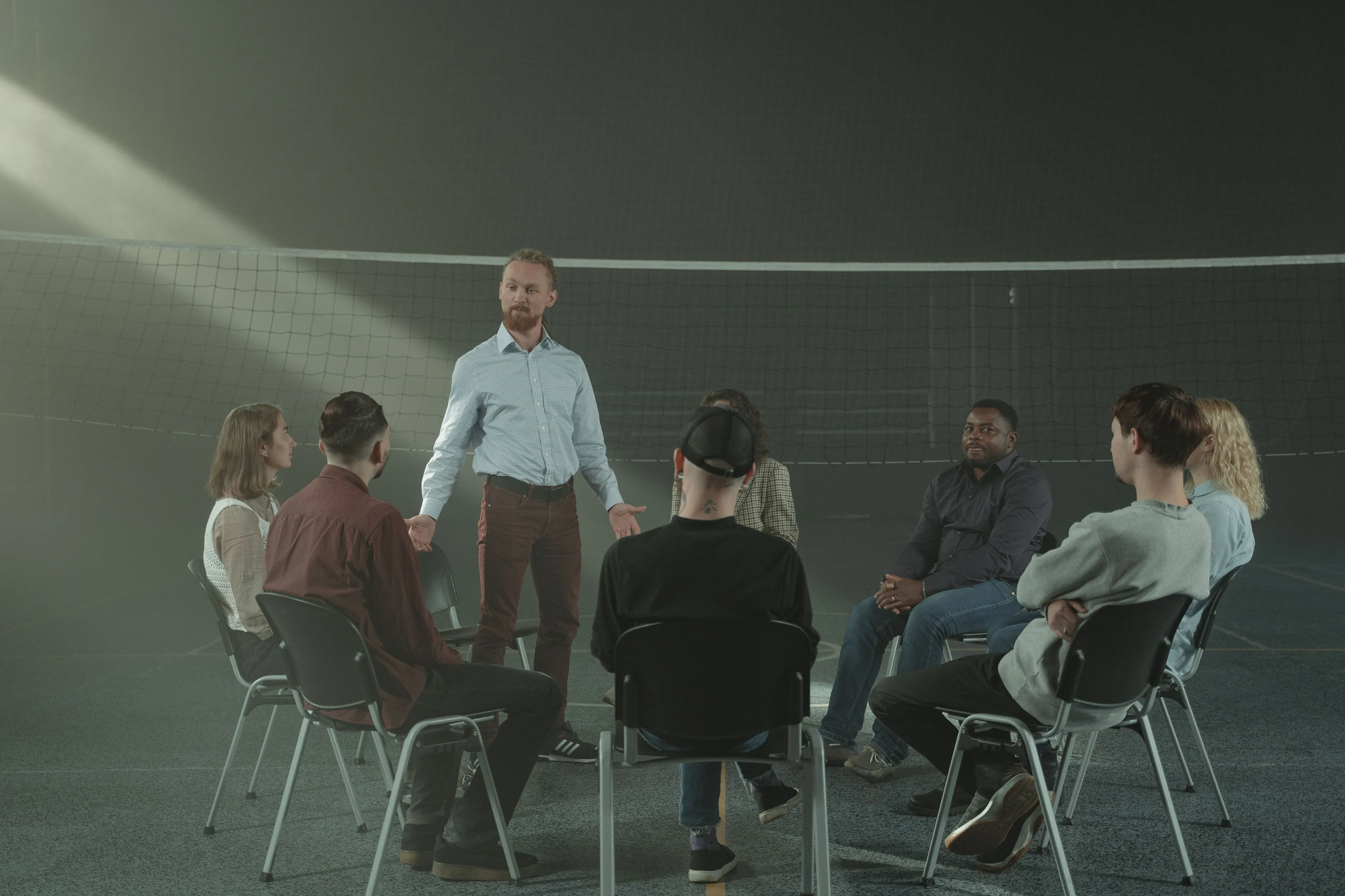 A group of people sitting in a circle listening to a man speaking, likely in an improv class.