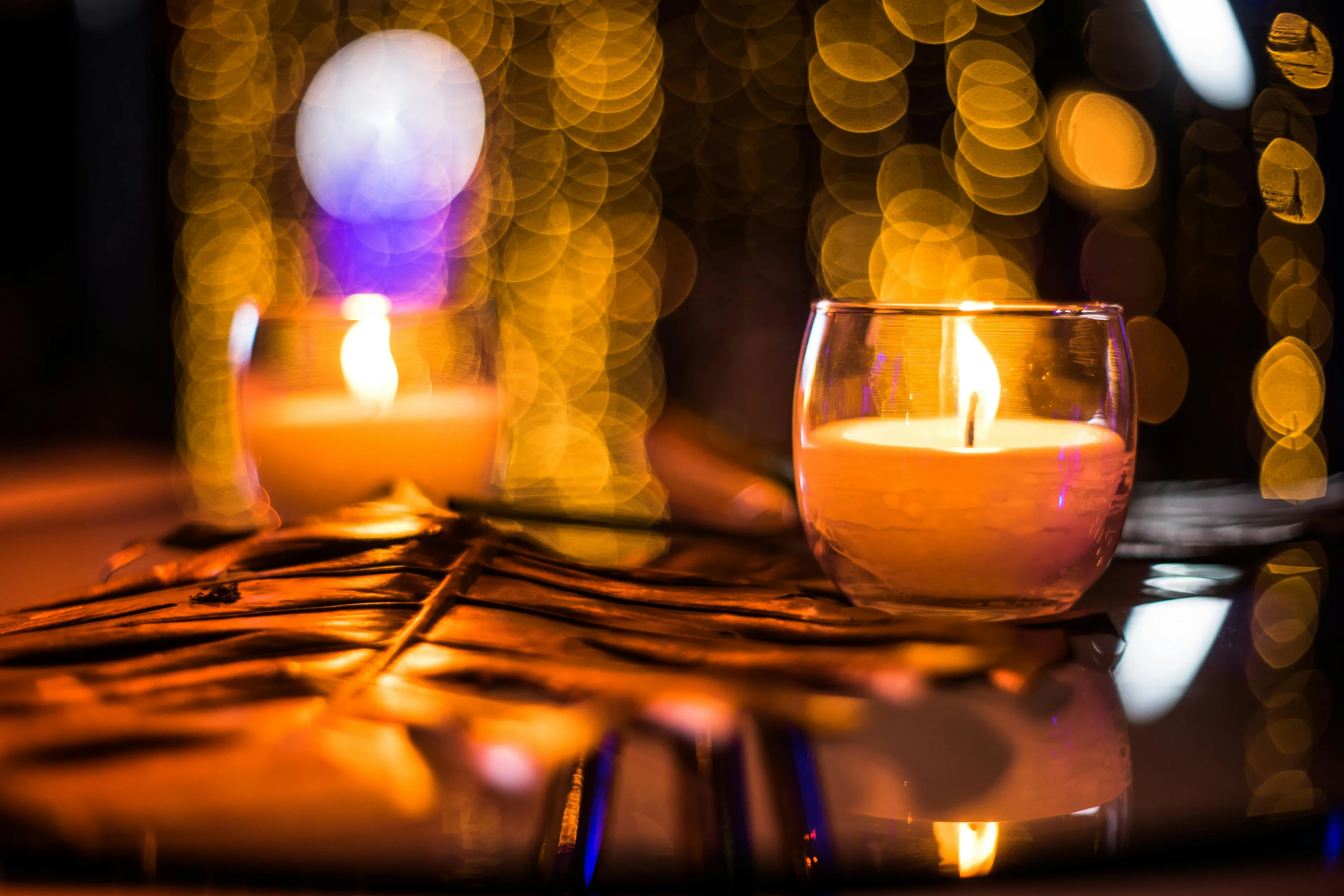 Two glowing candlelight candles in glass holders with a backdrop of warm, blurred bokeh lights.