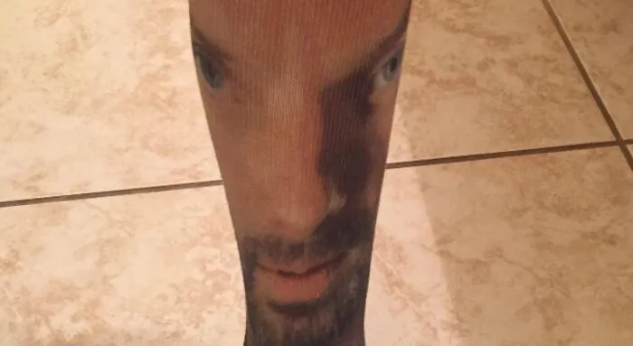 A sock with a man's face printed on it, stretched and distorted on a leg, showing bad clothing designs.