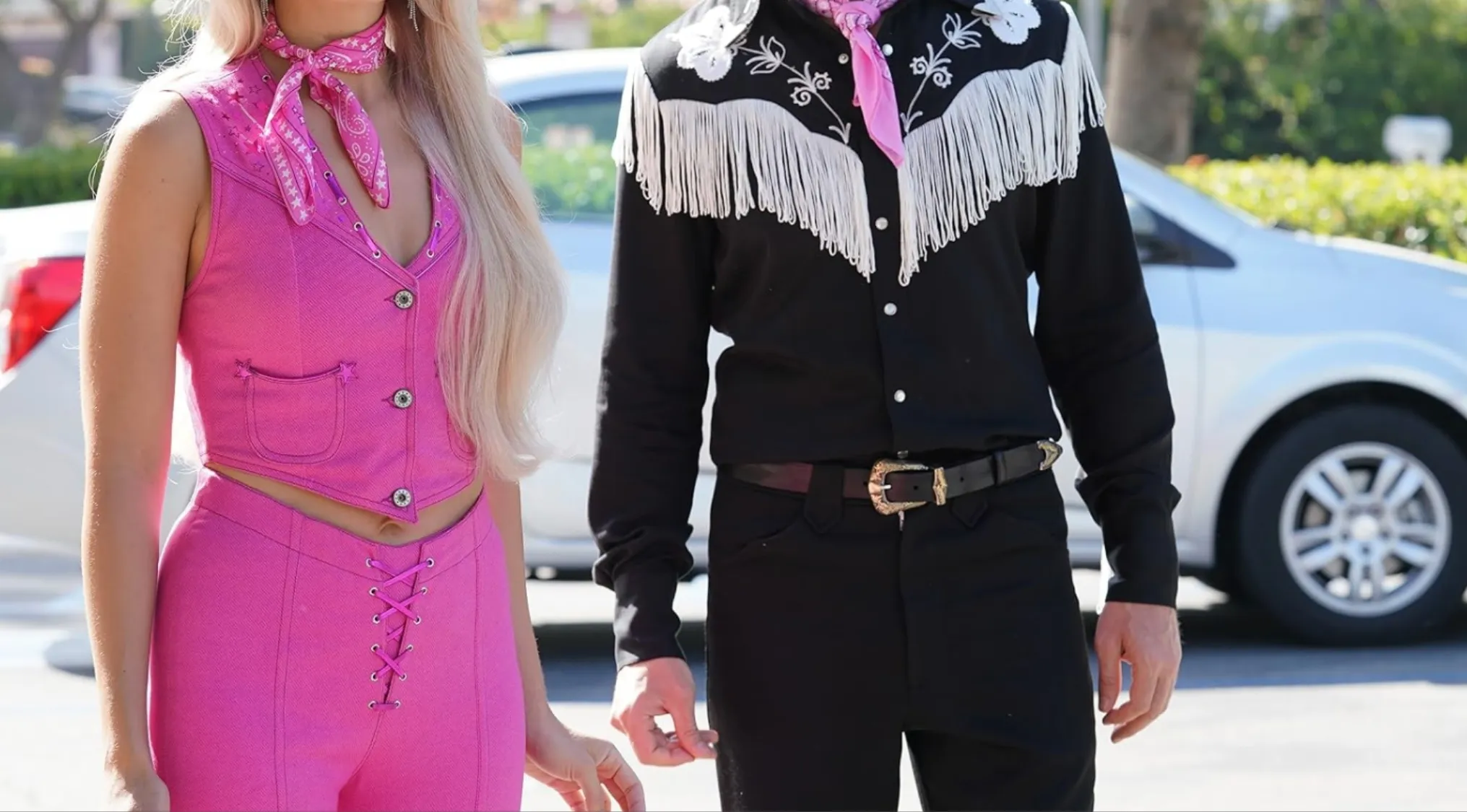 Pink vest and pants with blonde hair next to a man in a black fringed cowboy shirt, both wearing pink bandanas. Iconic outfits from a modern pop-culture film.