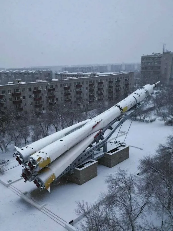 A snow-covered rocket monument surrounded by grey apartment buildings