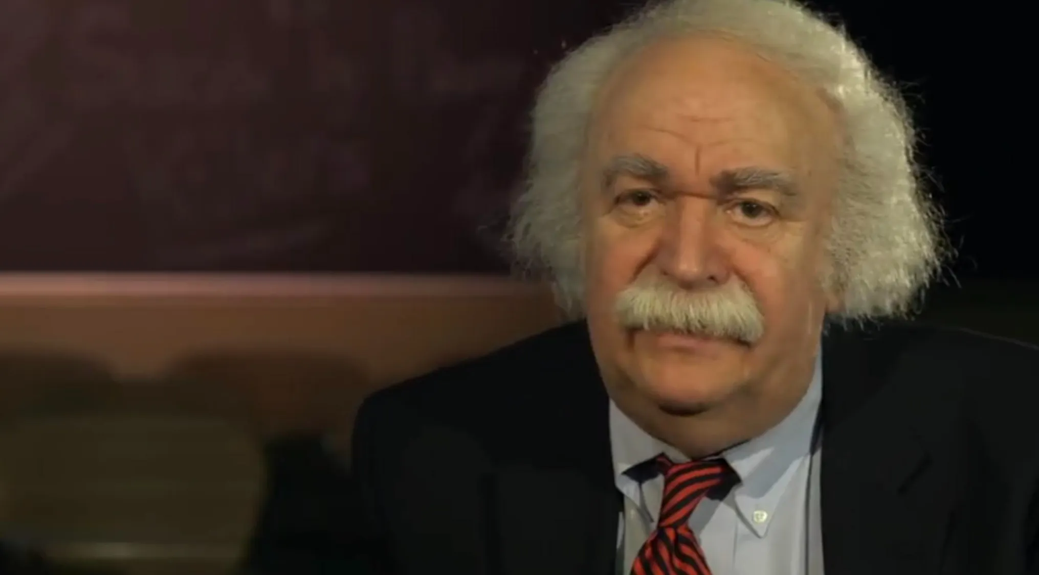 A man with white curly hair and a mustache, wearing a suit and tie. A Celebrity doppelganger, who does this man look like?