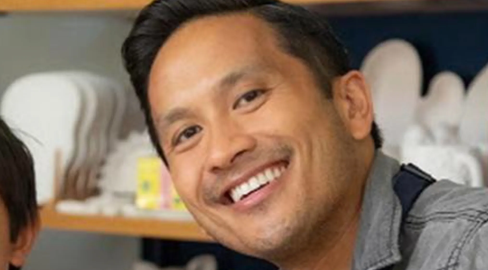 A man smiling, his head tilted. He has short dark hair, warm brown eyes, and a neat beard. Is he a celebrity doppelganger?