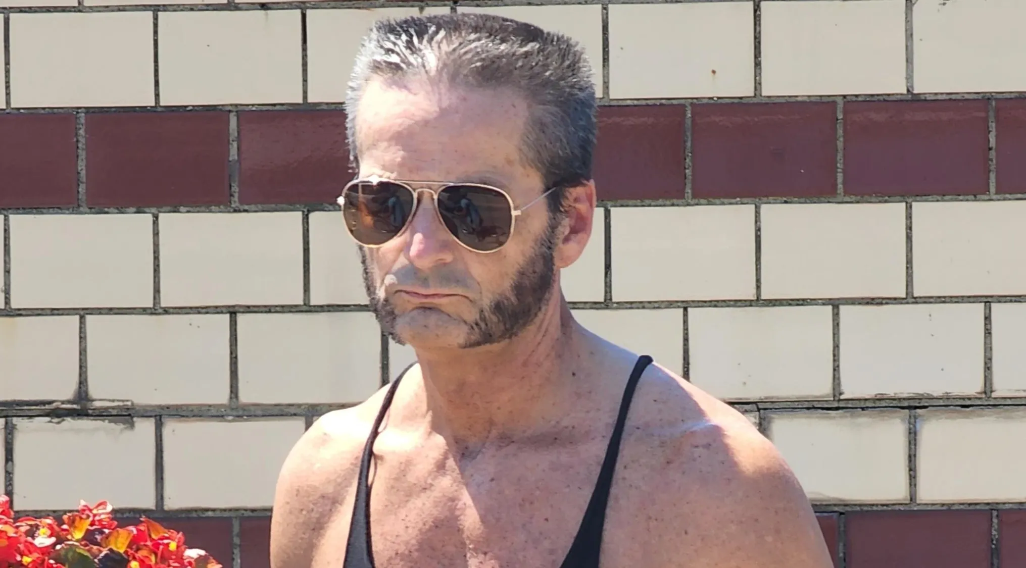 A man with prominent sideburns, sunglasses, and a black tank top, posing for Celebrity Doppelgangers.