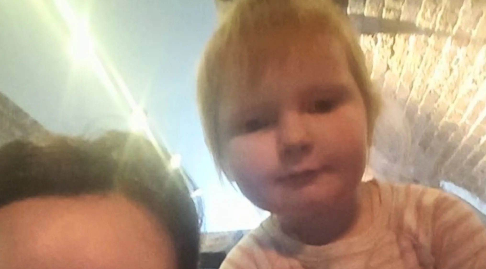 A close-up selfie of a curious blonde-haired baby girl, potentially a celebrity doppelganger, looking at the camera.