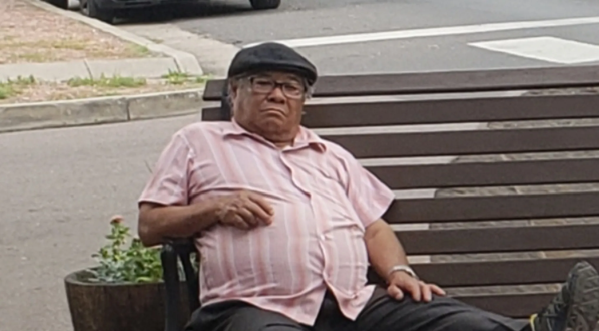 A man wearing a flat cap and glasses, sitting on a park bench. Celebrity doppelgangers: Who does this person remind you of?