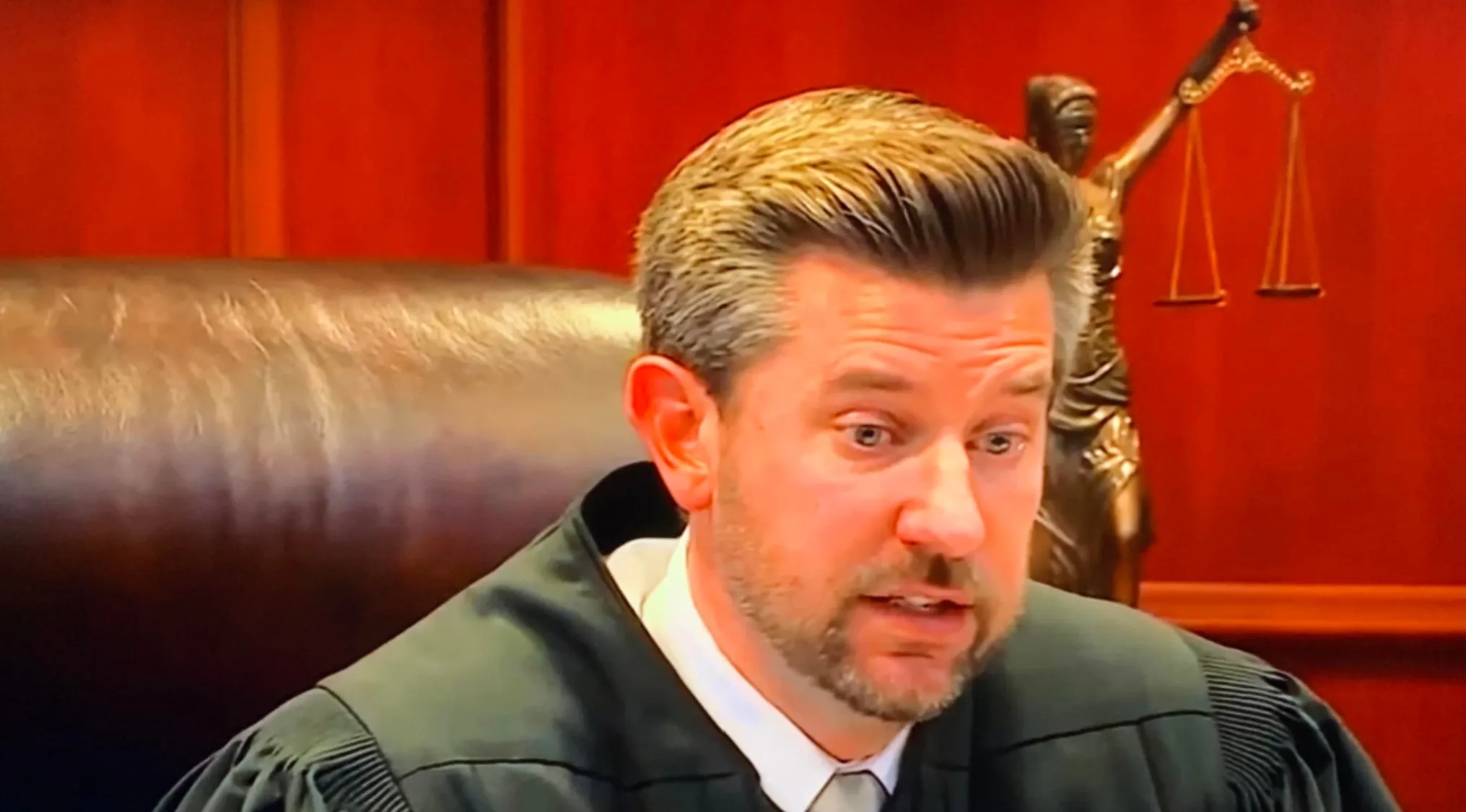 A male judge with neatly styled hair and a beard, in a robe and tie, hinting at celebrity doppelgangers.
