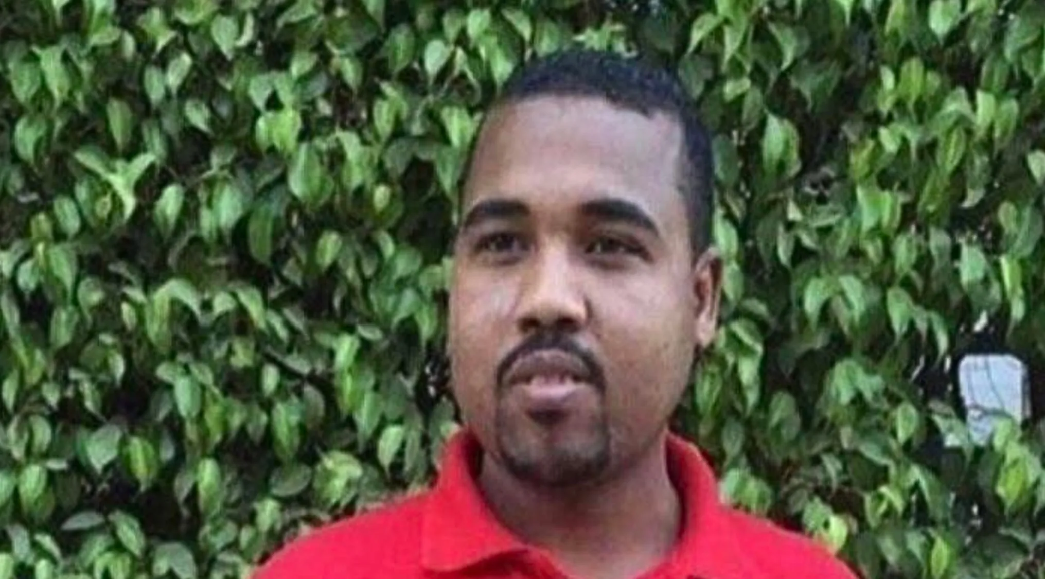 A man in a red polo shirt against a green leafy background. Is he a celebrity doppelganger?