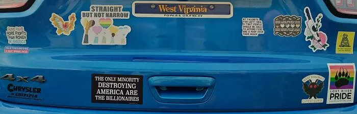 A blue car's bumper displays several funny bumper stickers, including political and pride-themed ones.