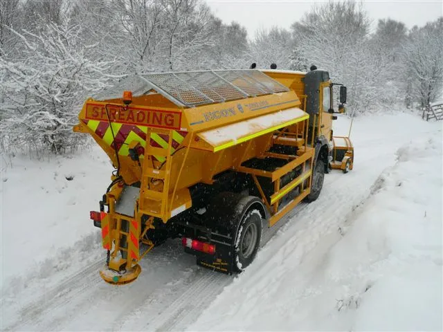 Large yellow salt spreading truck on a snowy road, clearing a path. Science behind salt on icy roads.