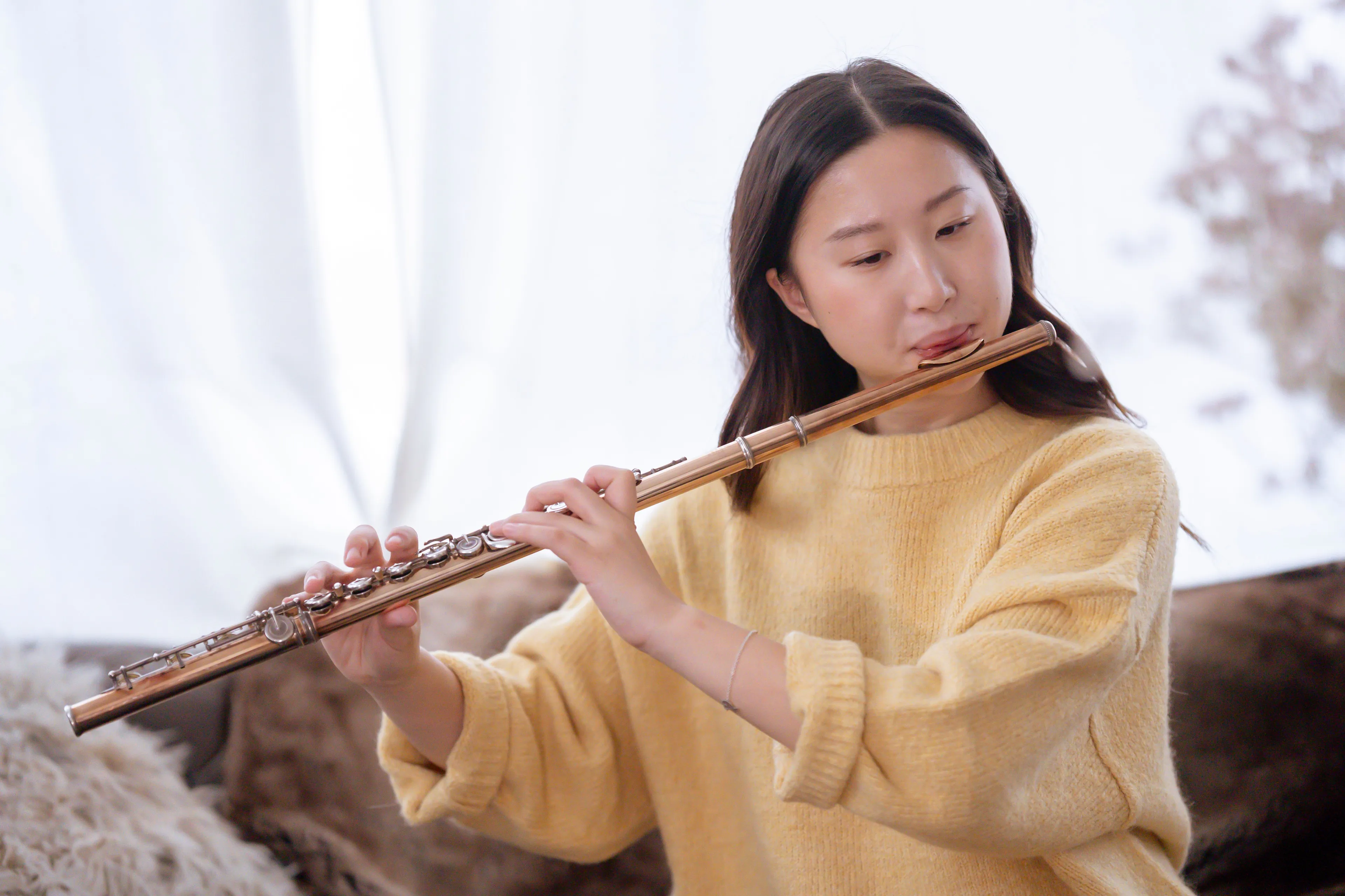 Young woman playing a flute, focused on the Art of music. She is wearing a yellow sweater.