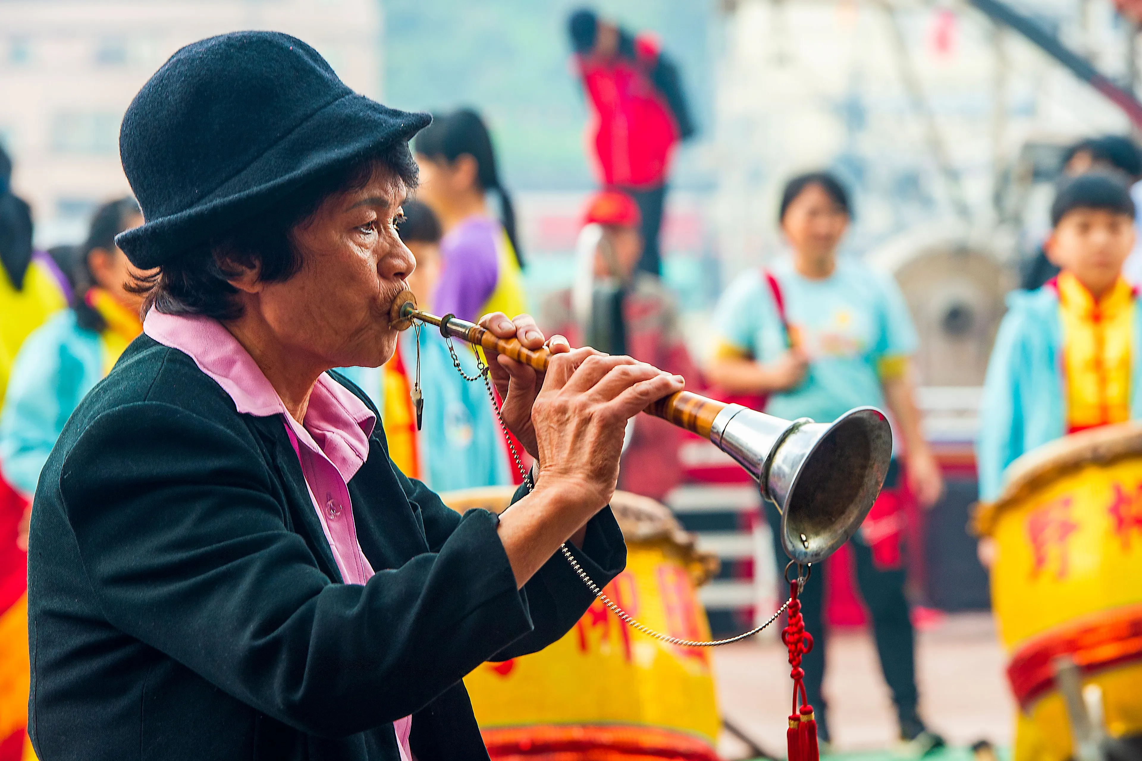 A person in a black hat plays a wind instrument like a bassoon, part of a cultural Art performance.