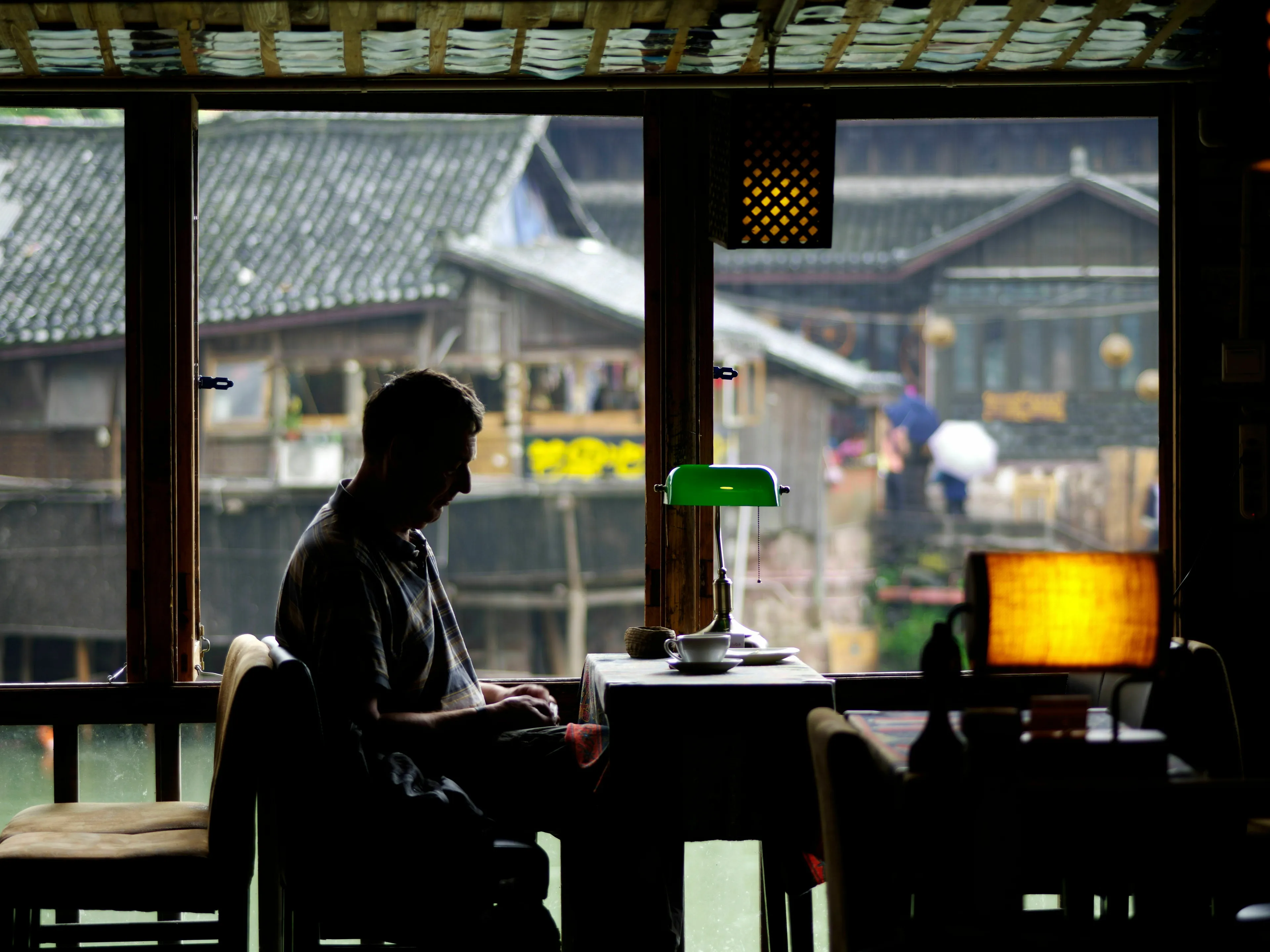 A man sitting alone at a restaurant table by a window, silhouette against a view of old buildings. How extroverted are you?