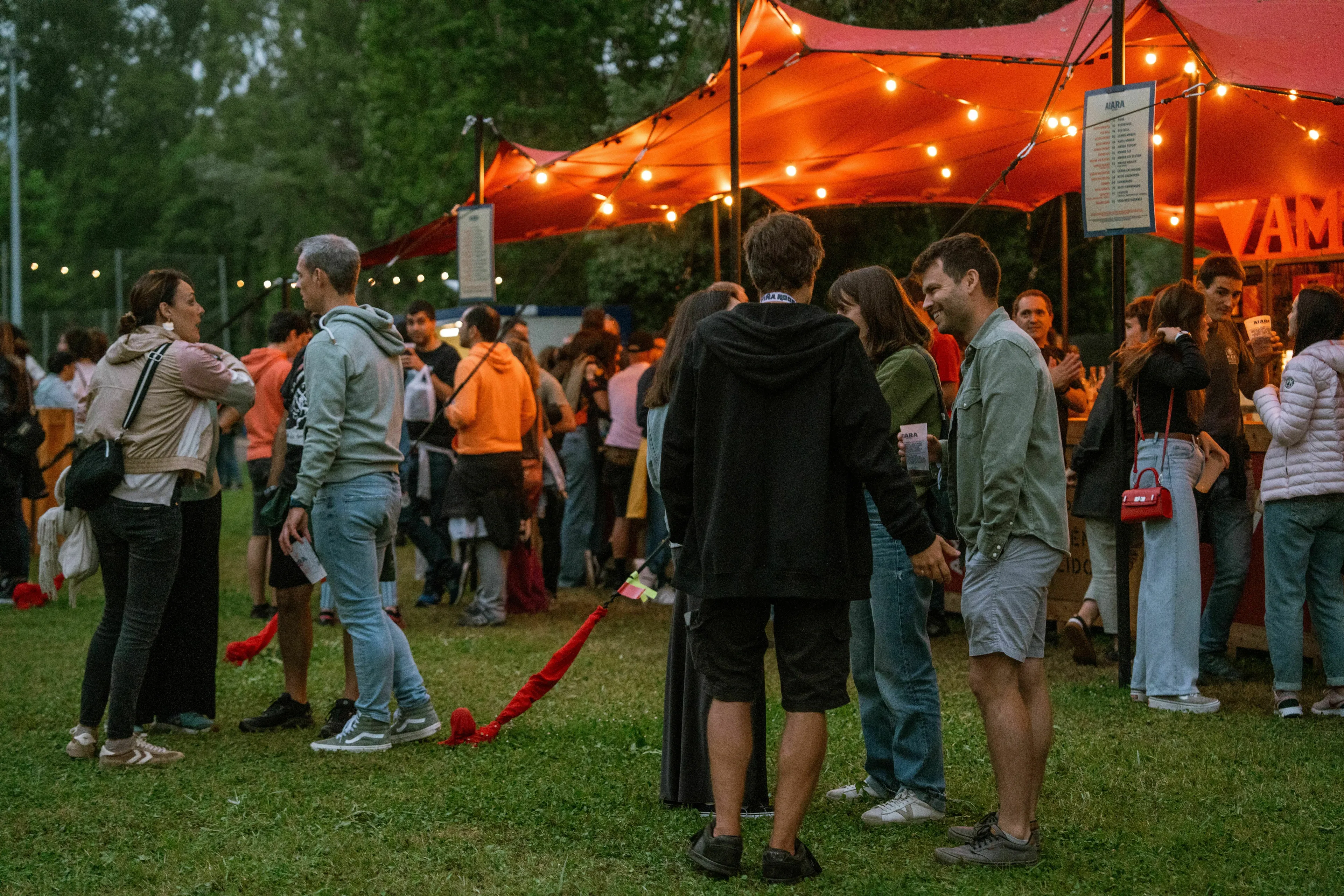 A lively social event at night with people gathered under a lit red tent, gauging how extroverted they are.