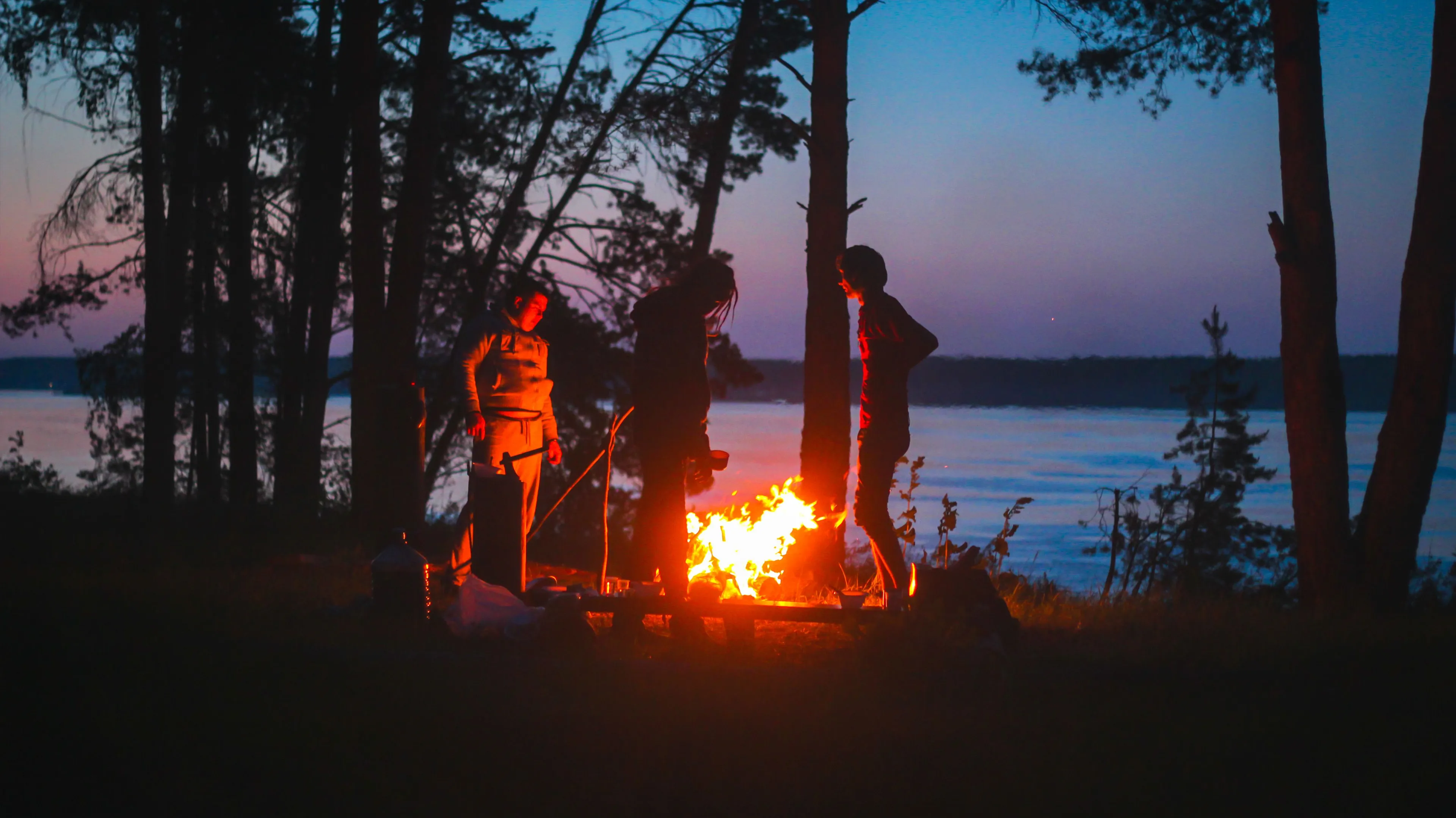 Friends gathered around a warm bonfire near a lake at dusk, enjoying the peaceful atmosphere while camping.