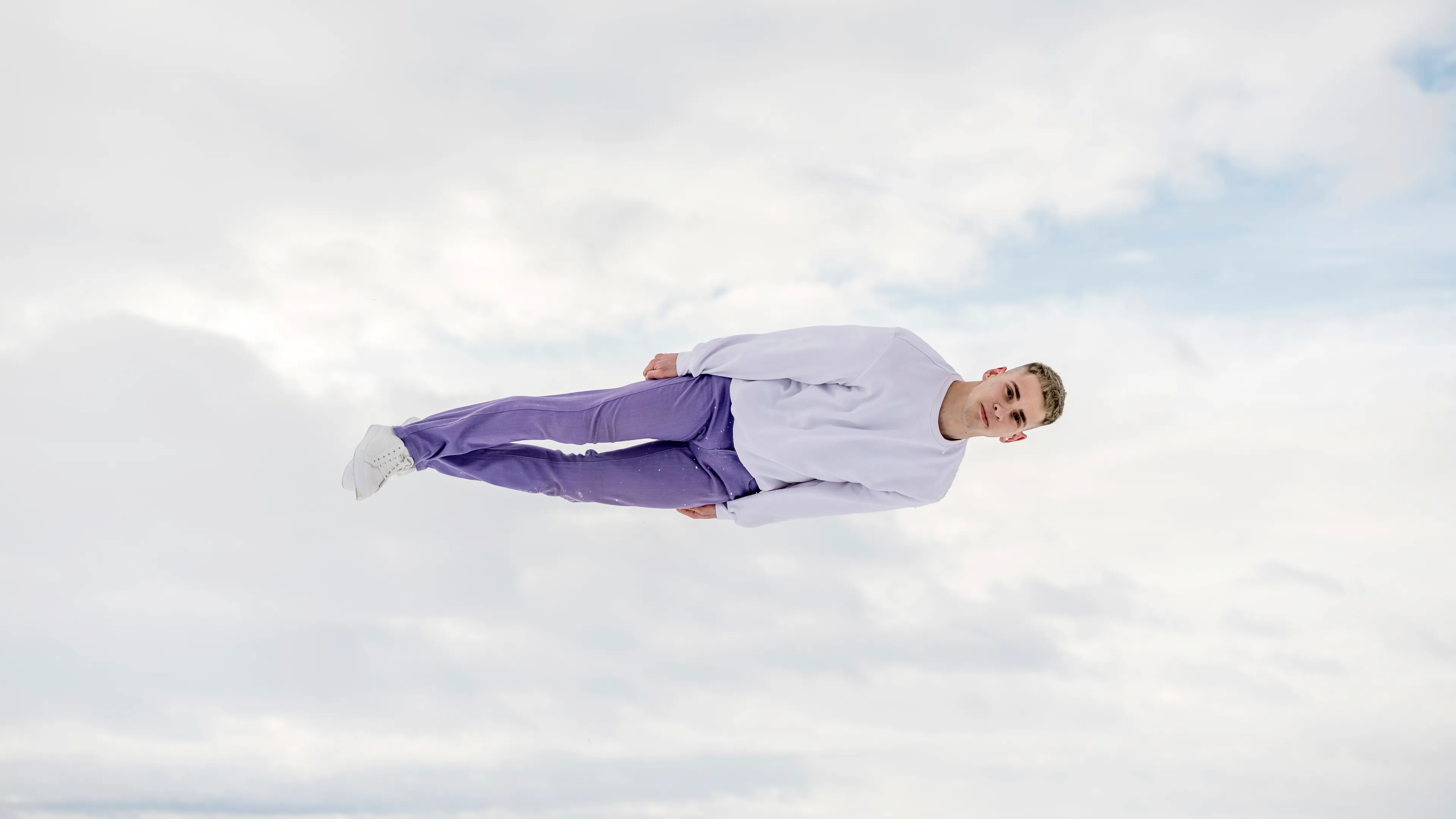 A young man in a white shirt and purple pants floating horizontally in the sky, demonstrating the superpower of flight.
