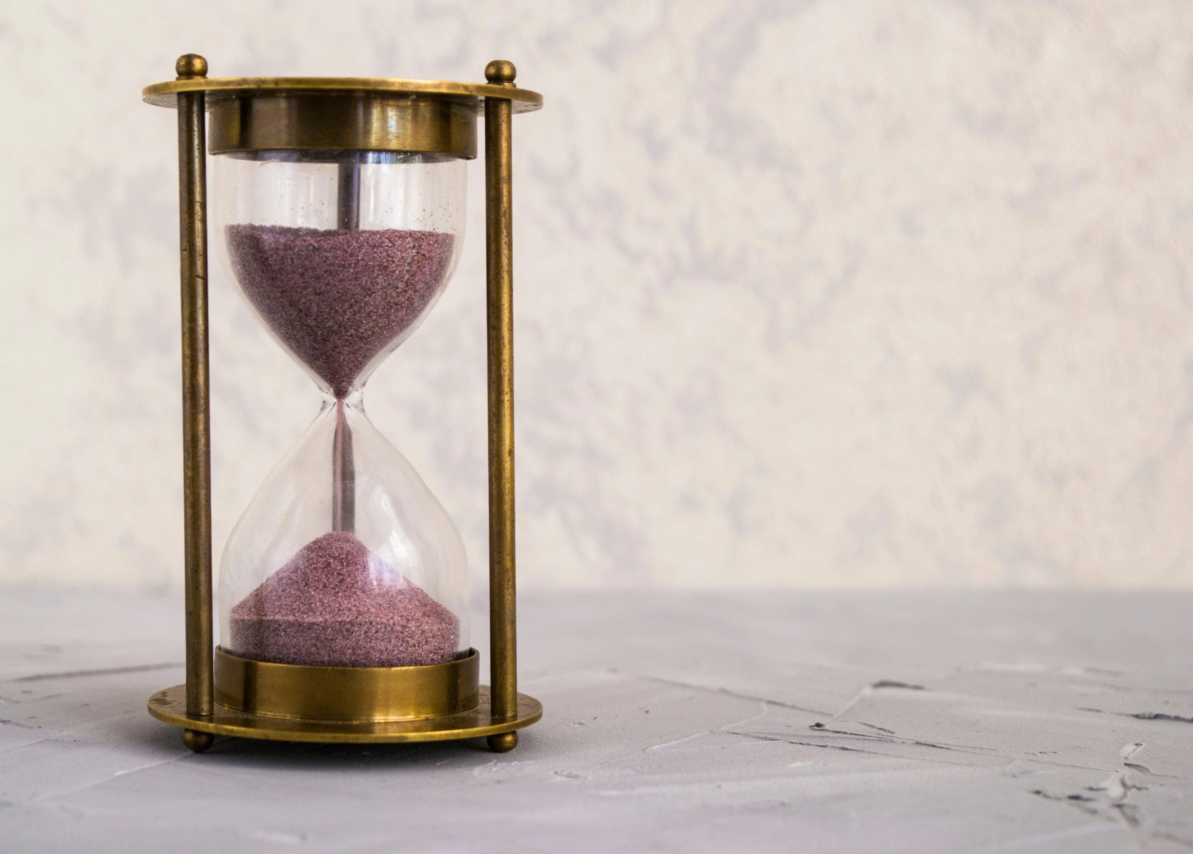 An hourglass with purple sand falling, against a textured light background, symbolizing the concept of time travel.