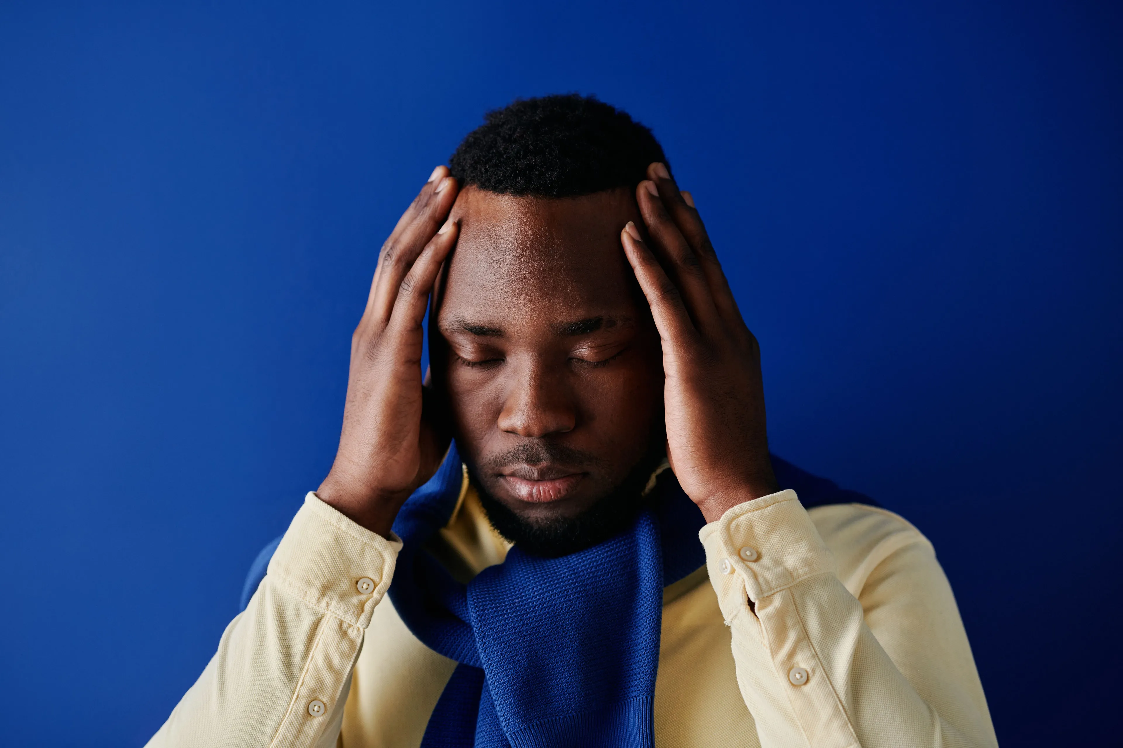 Man with eyes closed and hands to his temples, wearing a yellow shirt and blue scarf, contemplating mind reading.