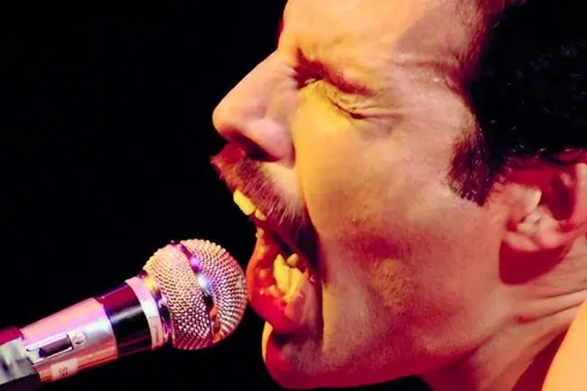 Freddie Mercury passionately singing into a microphone, eyes closed and mouth wide open, performing live.