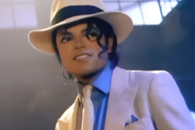Michael Jackson in a white fedora and suit, with a blue shirt and tie, looking slightly to the right.