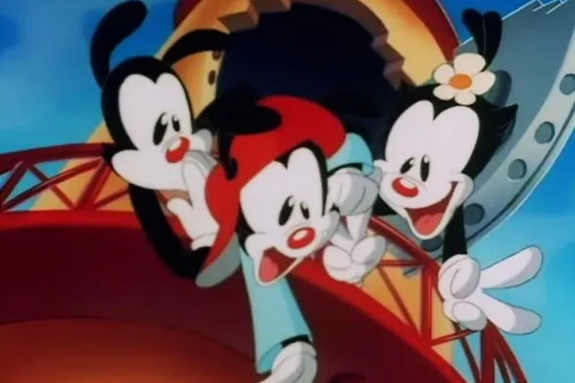 The Animaniacs, Wakko, Yakko, and Dot, are seen in a Saturday morning cartoon scene, smiling enthusiastically.