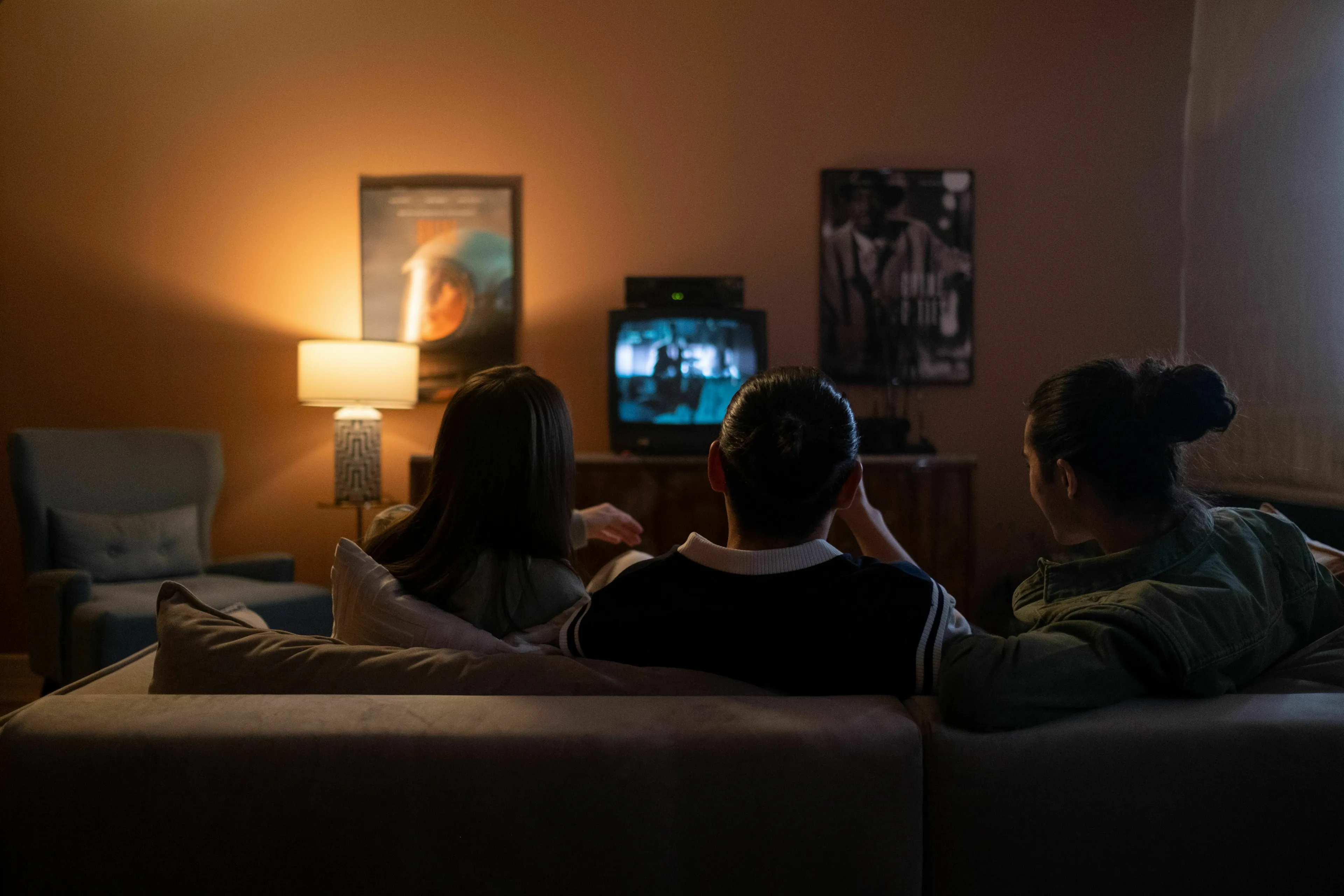 Three people binge-watching a show on an old TV in a dimly lit room, discussing pop culture.