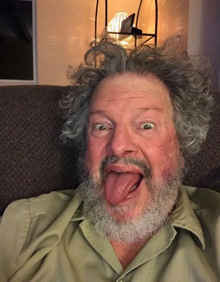 An amazing father with wild hair and a beard sticking out his tongue, displaying fun parents personality.