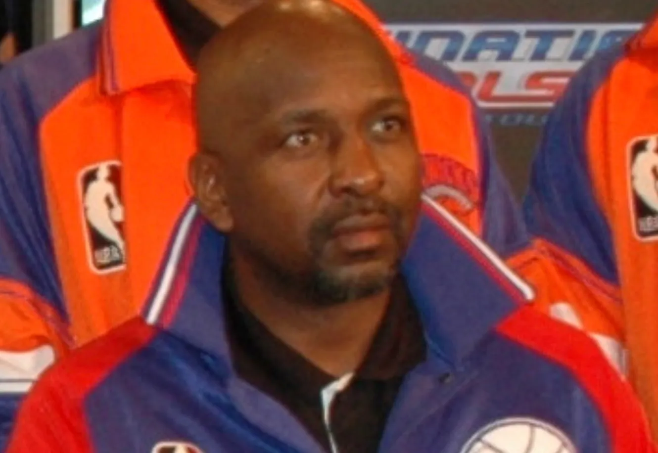 Close-up of Moses Malone, legendary basketball player, wearing a blue and orange jacket with the NBA logo.
