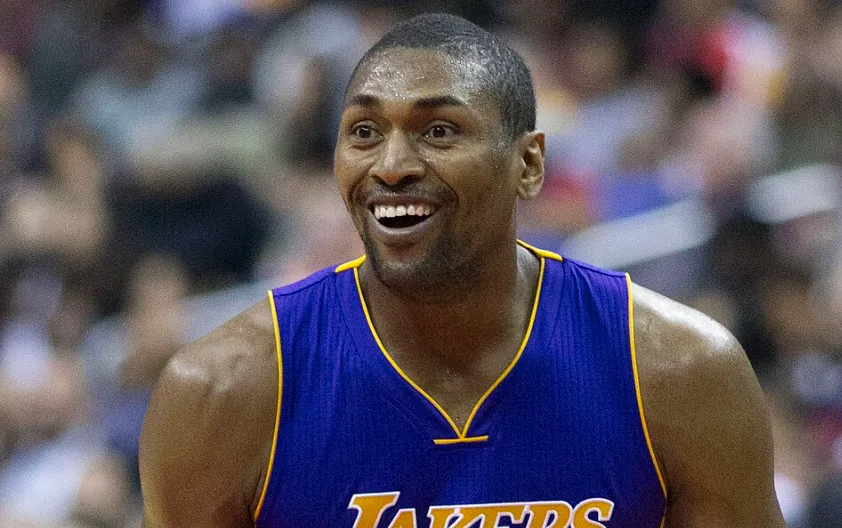 Metta World Peace in a purple Lakers jersey, smiling with an open mouth, during a basketball game.
